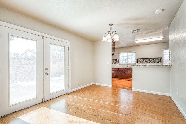 unfurnished dining area with french doors, light hardwood / wood-style flooring, a notable chandelier, and sink