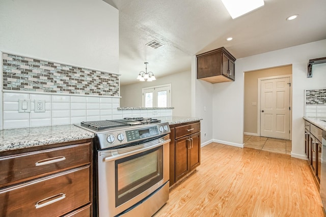 kitchen with tasteful backsplash, light stone countertops, stainless steel gas stove, and light hardwood / wood-style floors