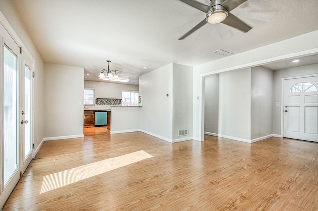 unfurnished living room featuring ceiling fan with notable chandelier, light hardwood / wood-style flooring, and a healthy amount of sunlight