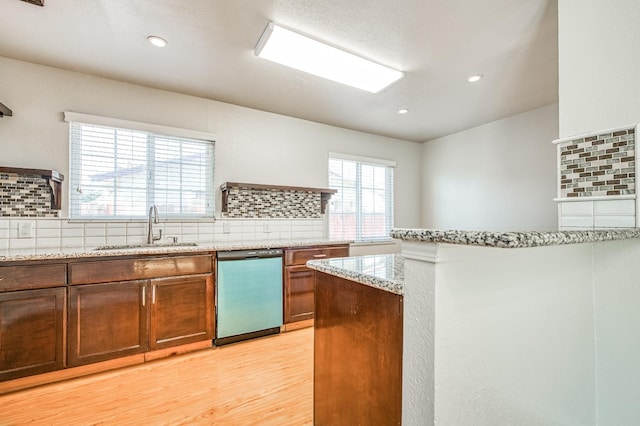 kitchen with tasteful backsplash, light stone counters, sink, light hardwood / wood-style floors, and dishwasher