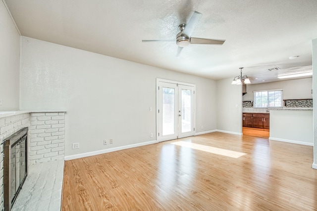 unfurnished living room featuring light wood-type flooring, ceiling fan with notable chandelier, a textured ceiling, and a fireplace