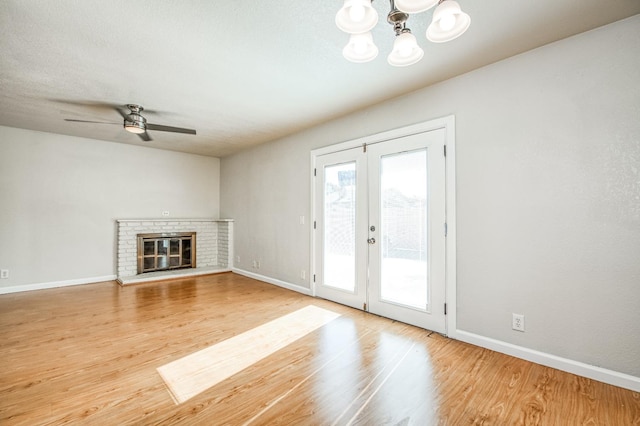 unfurnished living room featuring french doors, hardwood / wood-style floors, a fireplace, and ceiling fan with notable chandelier