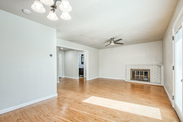 unfurnished living room featuring ceiling fan with notable chandelier, light hardwood / wood-style floors, and a brick fireplace