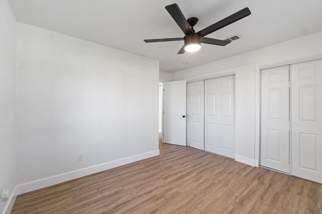 unfurnished bedroom featuring multiple closets, visible vents, a ceiling fan, light wood-type flooring, and baseboards