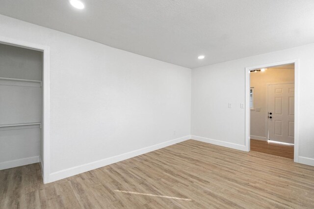 unfurnished bedroom with recessed lighting, baseboards, light wood-style floors, a spacious closet, and a closet