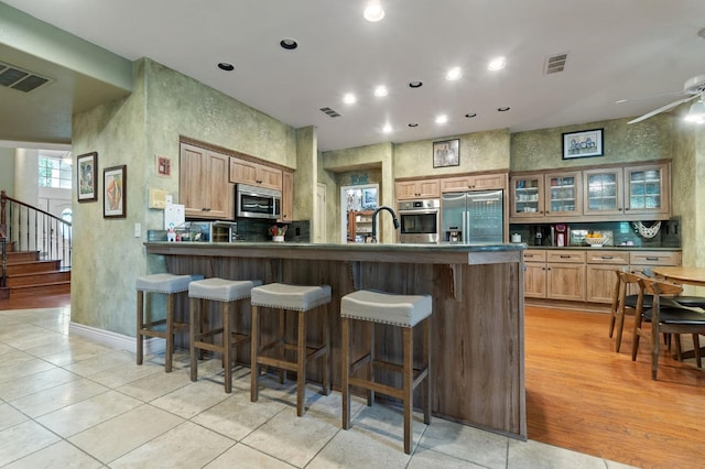 kitchen featuring ceiling fan, stainless steel appliances, kitchen peninsula, a breakfast bar, and light wood-type flooring