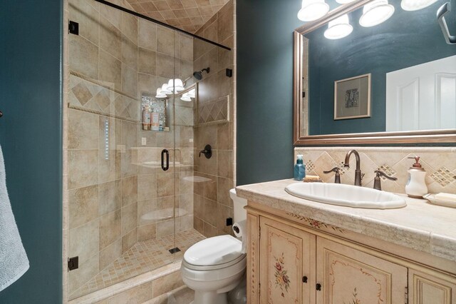 bathroom with backsplash, a shower with door, vanity, and toilet