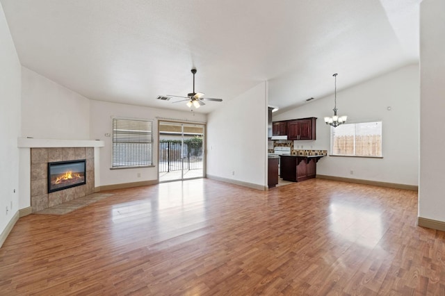 unfurnished living room featuring light wood-type flooring, a tiled fireplace, lofted ceiling, and ceiling fan with notable chandelier