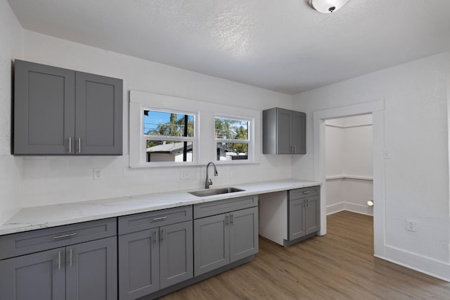 kitchen featuring sink, tasteful backsplash, light stone countertops, dark hardwood / wood-style floors, and gray cabinets