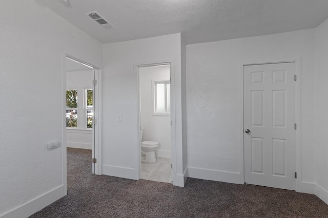 unfurnished bedroom featuring ensuite bathroom, dark colored carpet, and a textured ceiling