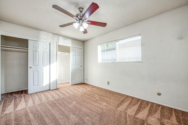 unfurnished bedroom with a textured ceiling, multiple closets, carpet floors, and ceiling fan