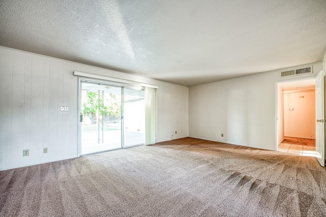 carpeted empty room with wood walls and a textured ceiling