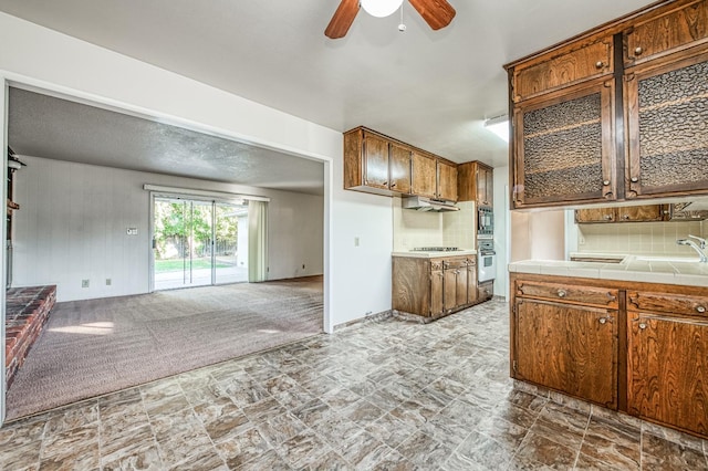 kitchen featuring tile counters, light colored carpet, sink, tasteful backsplash, and ceiling fan