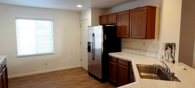 kitchen with tile countertops, stainless steel fridge with ice dispenser, sink, and wood-type flooring