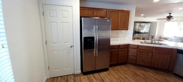 kitchen featuring stainless steel appliances, sink, ceiling fan, light hardwood / wood-style flooring, and tile counters