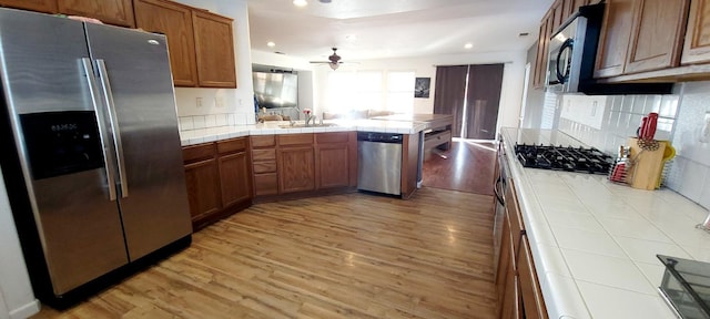 kitchen with tile countertops, appliances with stainless steel finishes, sink, and light hardwood / wood-style floors