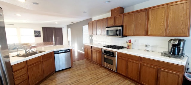 kitchen with stainless steel appliances, tile countertops, sink, and light wood-type flooring