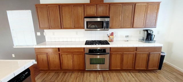 kitchen with tile countertops, appliances with stainless steel finishes, and light hardwood / wood-style floors