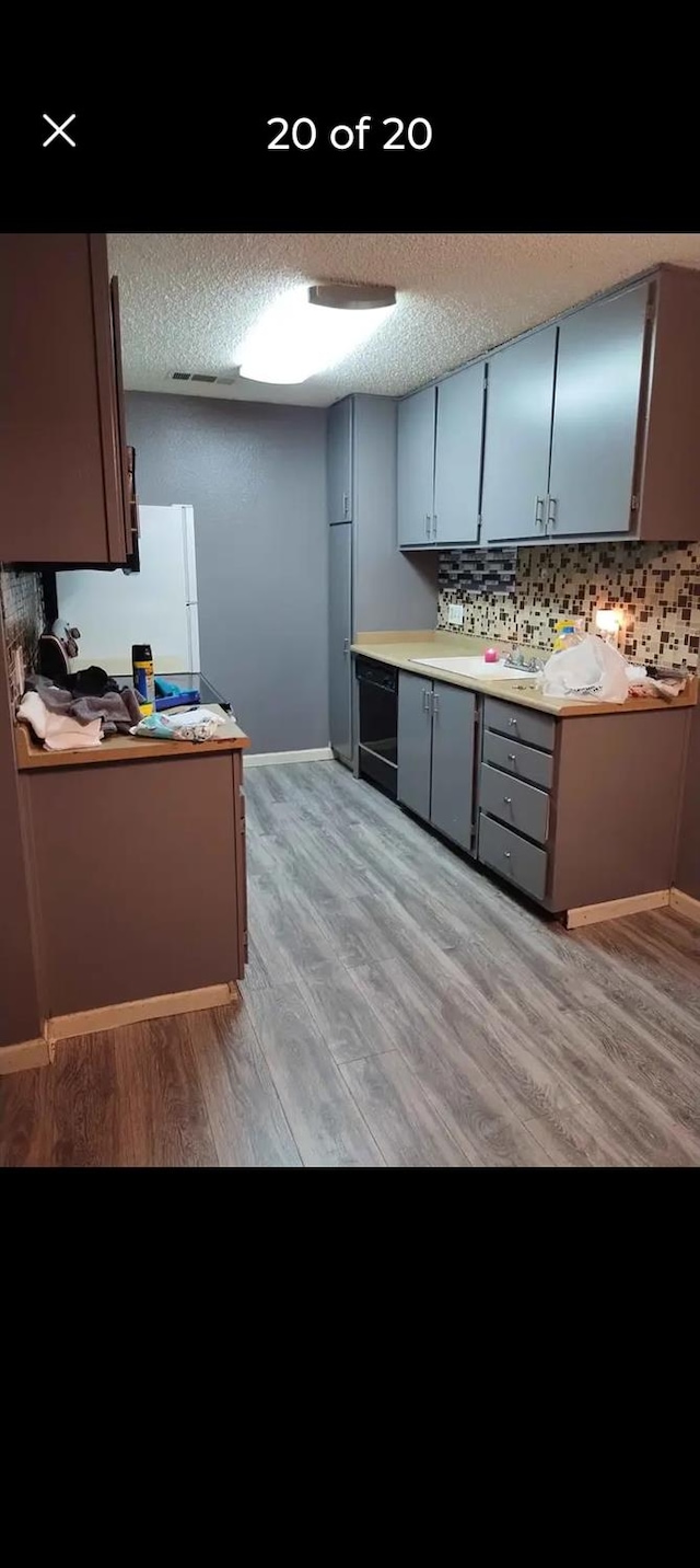 kitchen featuring light wood-type flooring, white refrigerator, a textured ceiling, and backsplash