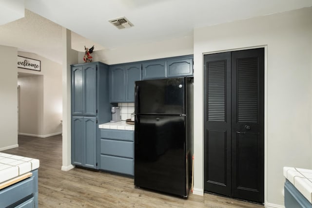 kitchen featuring black refrigerator, light wood-type flooring, tile countertops, and blue cabinets