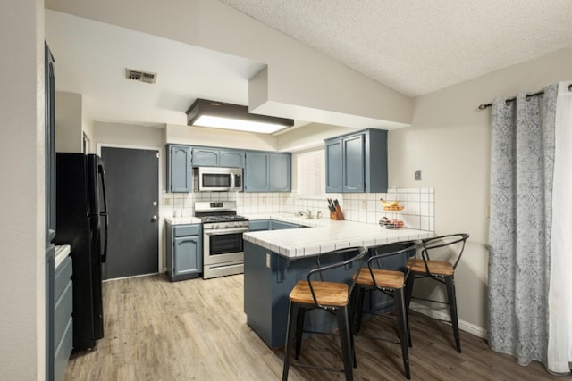 kitchen with a kitchen breakfast bar, light wood-type flooring, appliances with stainless steel finishes, tasteful backsplash, and kitchen peninsula