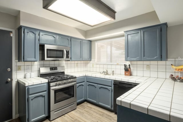 kitchen featuring appliances with stainless steel finishes, backsplash, light hardwood / wood-style floors, and tile counters