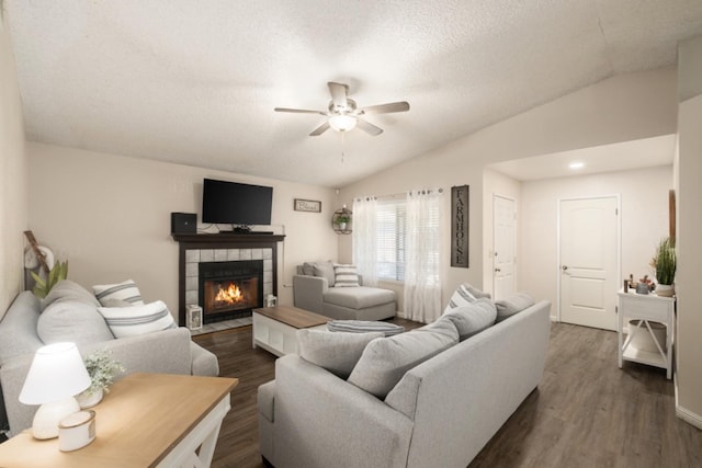 living room featuring lofted ceiling, a tile fireplace, dark hardwood / wood-style floors, ceiling fan, and a textured ceiling