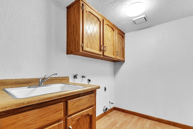 washroom with hookup for a washing machine, cabinets, sink, light hardwood / wood-style floors, and electric dryer hookup