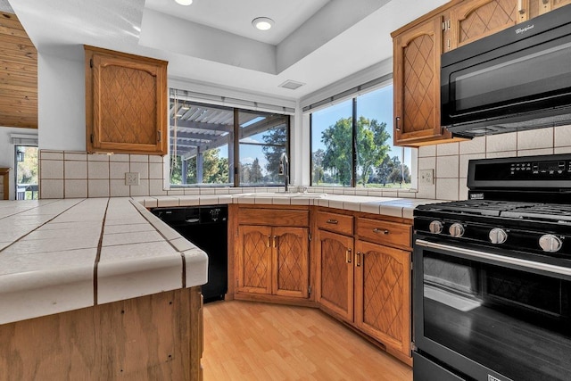 kitchen with tile countertops, black appliances, and a healthy amount of sunlight