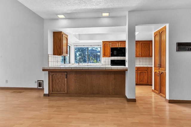 kitchen featuring black appliances, backsplash, a textured ceiling, tile counters, and light hardwood / wood-style flooring