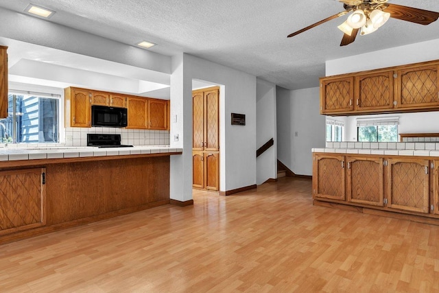 kitchen with tile counters, a healthy amount of sunlight, black appliances, and light hardwood / wood-style floors