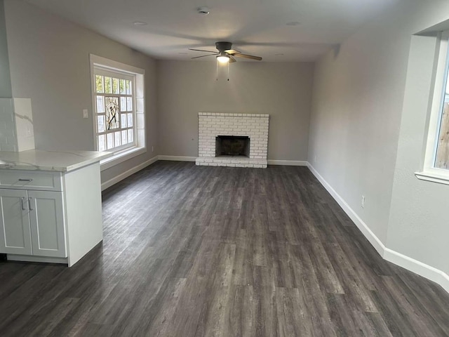 unfurnished living room featuring ceiling fan, a brick fireplace, and dark hardwood / wood-style flooring