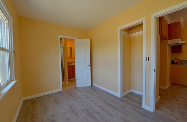 unfurnished bedroom featuring multiple windows, light wood-type flooring, and a walk in closet