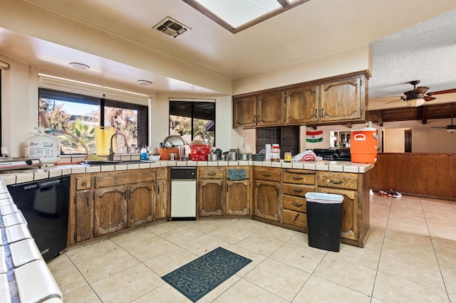 kitchen featuring kitchen peninsula, ceiling fan, light tile patterned floors, tile countertops, and dishwasher