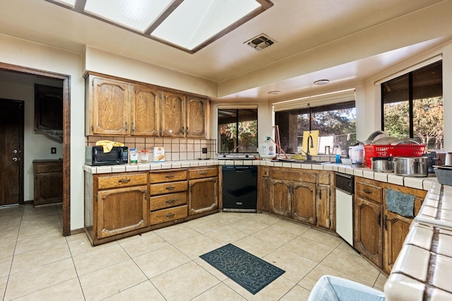 kitchen featuring decorative backsplash, black appliances, sink, tile counters, and light tile patterned flooring