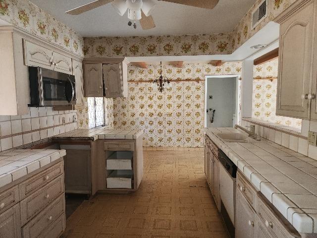 kitchen with tile counters, ceiling fan, sink, and dishwasher