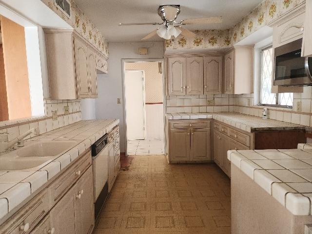 kitchen with white dishwasher, light brown cabinetry, sink, tile counters, and ceiling fan