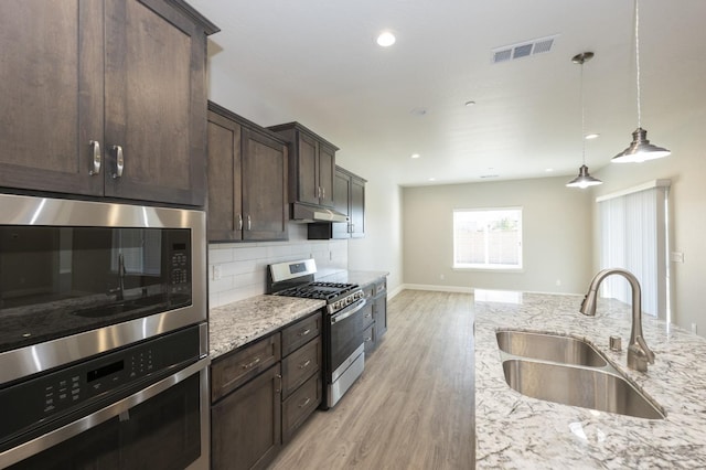 kitchen featuring stainless steel appliances, sink, light stone countertops, dark brown cabinets, and light hardwood / wood-style flooring