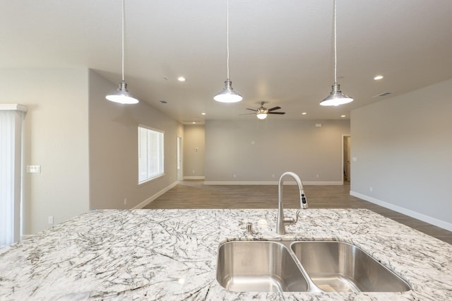 kitchen with hardwood / wood-style flooring, sink, light stone countertops, ceiling fan, and pendant lighting