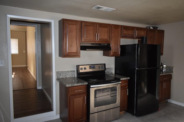 kitchen with stainless steel electric stove, light tile patterned flooring, black fridge, and light stone countertops