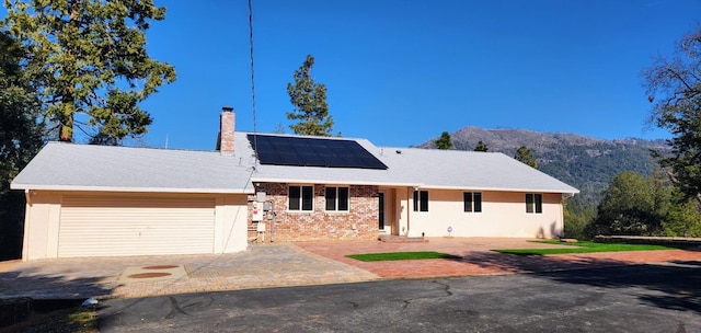 single story home featuring a garage, a mountain view, and solar panels