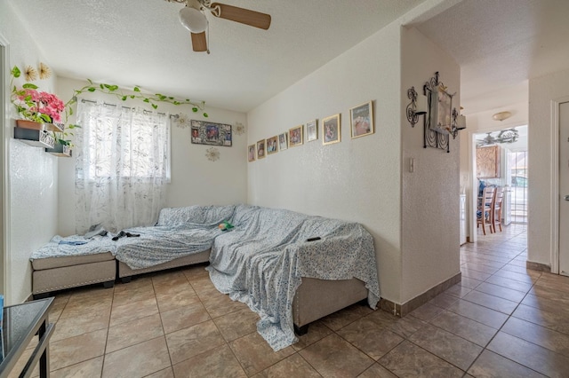 living area featuring a textured wall, tile patterned flooring, a ceiling fan, and a healthy amount of sunlight