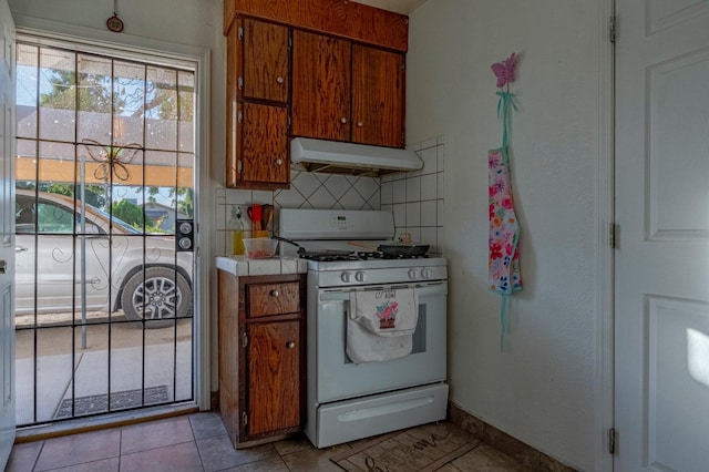 kitchen with tile counters, white gas range, brown cabinets, decorative backsplash, and extractor fan