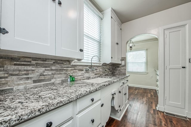 kitchen featuring a wealth of natural light, light stone countertops, sink, and white cabinets