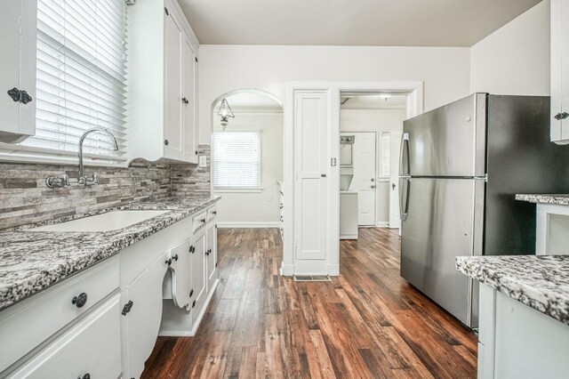 kitchen with backsplash, stainless steel refrigerator, sink, and white cabinets