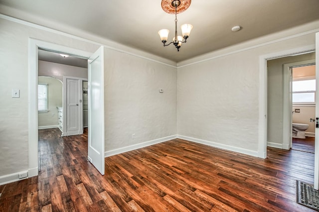 spare room featuring a notable chandelier, crown molding, and dark wood-type flooring