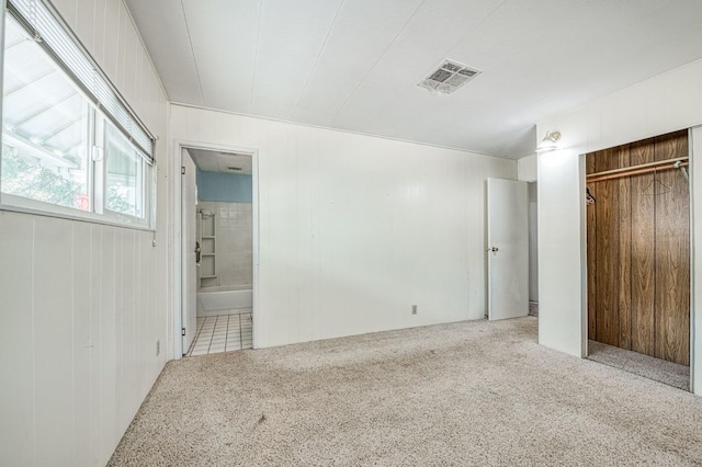 unfurnished bedroom with a closet, ensuite bath, wood walls, and light colored carpet