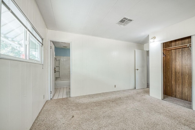 unfurnished bedroom featuring a closet, ensuite bathroom, carpet floors, wood walls, and visible vents