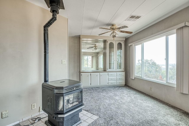interior space with a wood stove, ceiling fan, and visible vents
