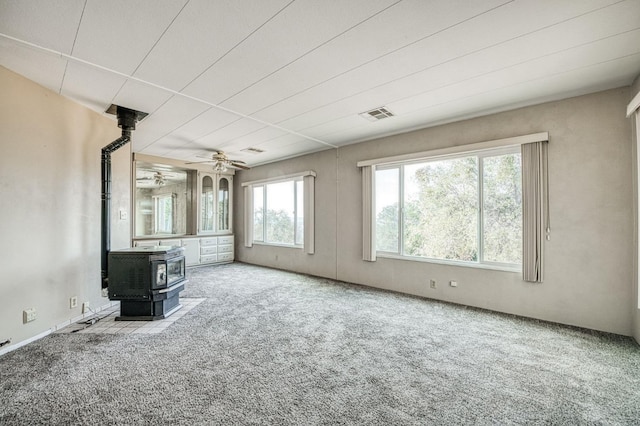 unfurnished living room with a wood stove, a ceiling fan, visible vents, and carpet floors